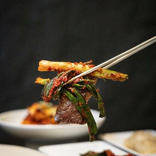 A piece of beef topped with green onion kimchi